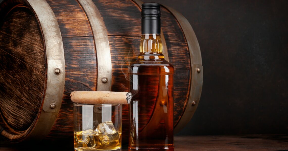 Scotch whiskey bottle, glass, cigar and old barrel